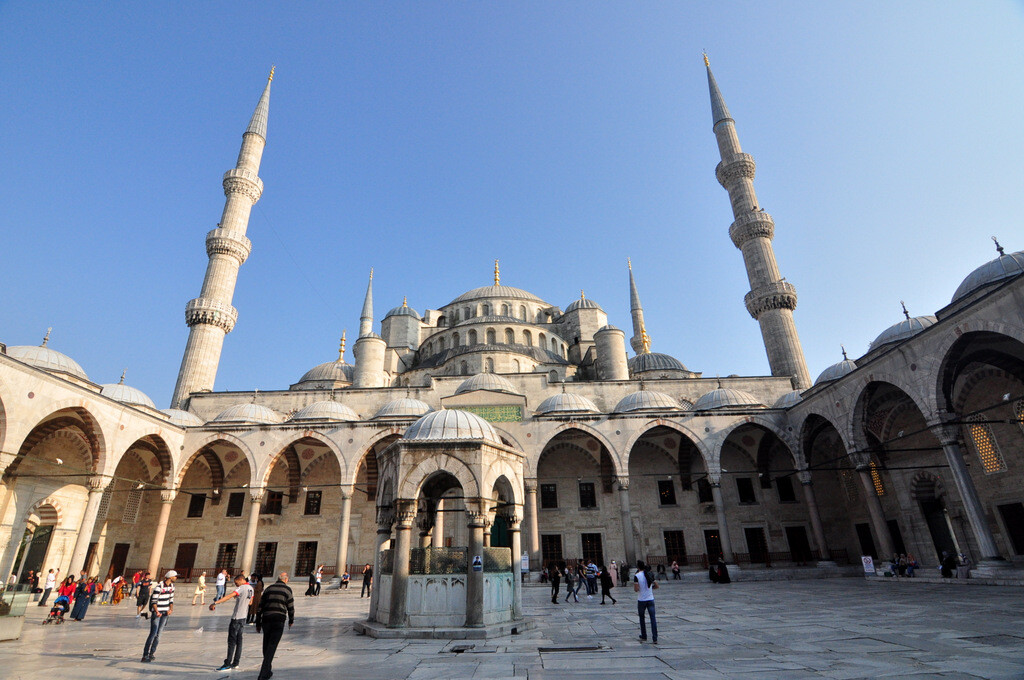 Visitors walking in the courtyard of the Blue Mosque while photographing the cascading domes of Sultanahmet Mosque